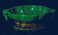 An even spinage green nephrite bowl, with black flecks, carved as a bowl with loose ring handles and a chrysanthemum style base.