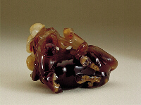 A rich dark brown chalcedony stone, with pale beige and almost white inclusions, brilliantly carved as a reclining horse with a couple of monkeys. One monkey is white, the other beige, and the horse is dark brown.