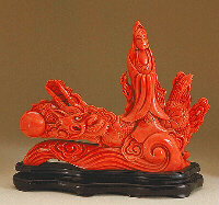 A large even coloured piece of Coral, carved as Guanyin, surrounded by a dragon and pearl riding above the waves.