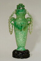 A double chained celadon green jadeite vase and cover. With dragon's head handles suspending loose rings to which each chain having ten loose double links are attached to the cover. Well hollowed, and splashes of emerald green well used to carve dragons in high relief.