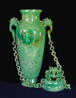 The Reverse: A double chained celadon green jadeite vase and cover. With dragon's head handles suspending loose rings to which each chain having ten loose double links are attached to the cover. Well hollowed, and splashes of emerald green well used to carve dragons in high relief.