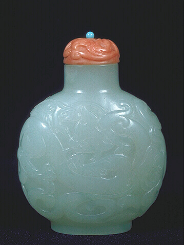 A muttonfat nephrite snuff bottle, well hollowed, carved in low relief with writhing dragons, a coral stopper. 