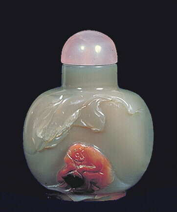 Chalcedony three colour snuff bottle, opaque brown with a russet and black inclusion carved to depict a cavernous cave with a crouched monkey holding a large black peach.