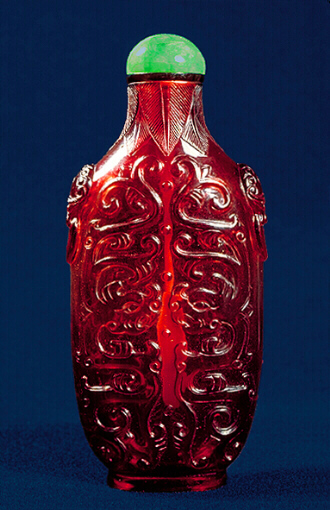 Glass Snuff Bottle, translucent ruby-red glass carved with writhing and confronting archaic dragons, the neck surrounded with palm fronds, the shoulders carved with mask ring handles.