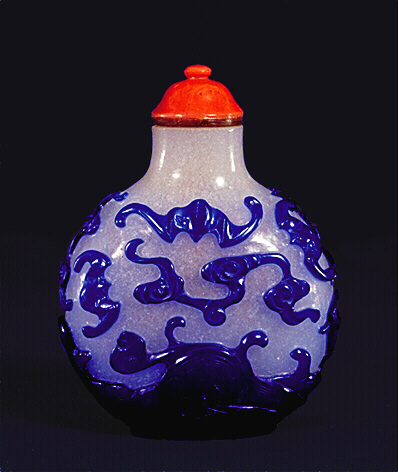 A snowflake ground glass snuff bottle with a sapphire-blue overlay carved with bats flying amongst clouds above turbulent waters.