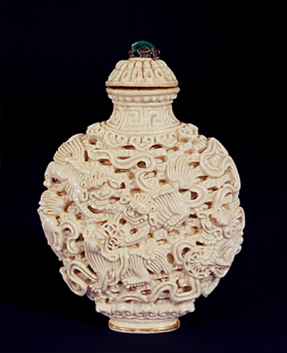 Porcelain snuff bottle, creamy-white enamel; moulded and reticulated with the design of Fo lions chasing beribboned brocade balls; set against a wave design the base and shoulders surrounded by ruyi lappets and the neck with a key-fret border; the base with an iron red Jiaqing mark.