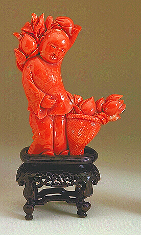 A good bright Coral carved as a figure of a young boy, carrying flowers on his back, with a basket of more flowers at his feet.