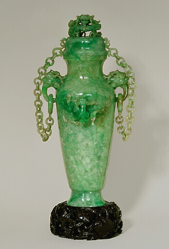 A double chained celadon green jadeite vase and cover. With dragon's head handles suspending loose rings to which each chain having ten loose double links are attached to the cover. Well hollowed, and splashes of emerald green well used to carve dragons in high relief.