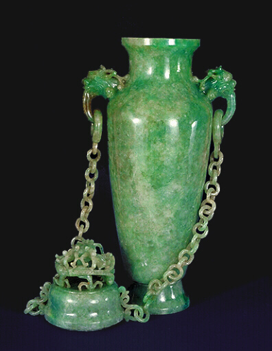 The Reverse: A double chained celadon green jadeite vase and cover. With dragon's head handles suspending loose rings to which each chain having ten loose double links are attached to the cover. Well hollowed, and splashes of emerald green well used to carve dragons in high relief.