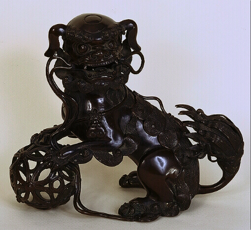 A Chinese bronze incense burner in the form of a fo lion with a ribboned brocade ball.