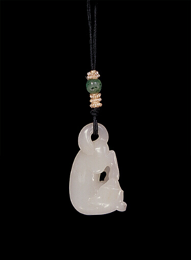 Nephrite pendant, mutton fat, carved in the form of a reclining dog with one rear paw in its mouth, its tail looped over onto its back to form the suspension area for the pendant.