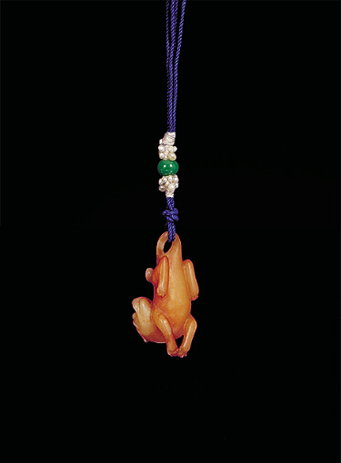 Base: Nephrite pendant, pale white with darker brown areas carved in miniature form showing a reclining dog, its head pointing backwards and its tale looped to receive the cord.