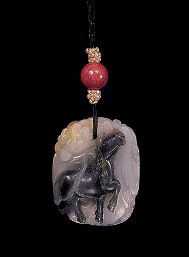 Nethrite pendant, mutton fat with dark grey and a little russet, carved with a prancing horse below pine trees and a monkey, on the other side is a grey monkey climbing white rocks near a black tree trunk.