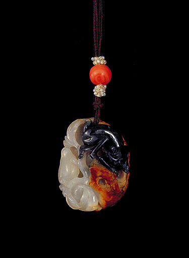 Nephrite pendant, of pebble form, the brown skin forming the outside of the pendant as rockwork, with a dark grey area carved as a climbing monkey with whiter areas representing peaches.