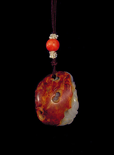 Reverse: Nephrite pendant, of pebble form, the brown skin forming the outside of the pendant as rockwork, with a dark grey area carved as a climbing monkey with whiter areas representing peaches.