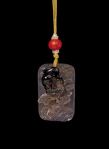 Chalcedony pendant, pale translucent stone with a darker brown skin, carved with a monkey scampering amongst the pine with a rockery below. The other side with craggy rockwork, pine and clouds and a raised inscription. Suzhou School.