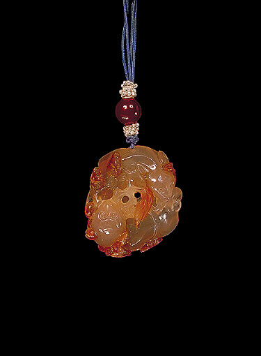 Chalcedony pendant, pale translucent orange agate with much darker russet areas carved with two feline animals curled up together with chrysanthemum flowers with leaves entwined around.