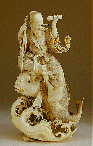 A fine ivory Okimono, carved from a solid tusk, of Kinko holding a scroll in one hand, and a staff in the other, whilst seated on a large carp above the waves.